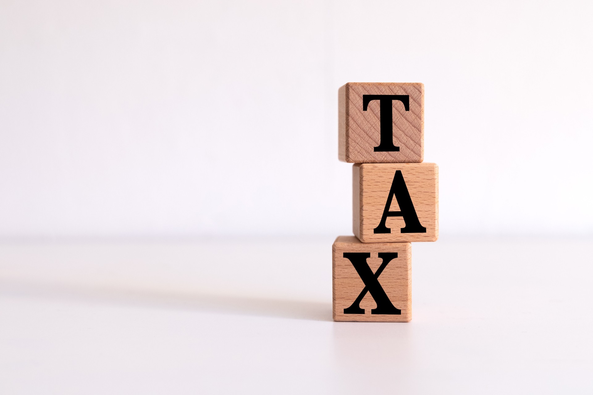 Three wooden cubes standing on top of each other with the letters TAX